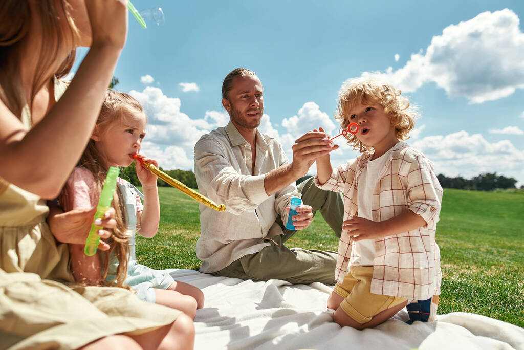 Милые маленькие дети веселятся, проводя время со своими родителями, семья устраивает пикник на природе в летний день - Фото, изображение