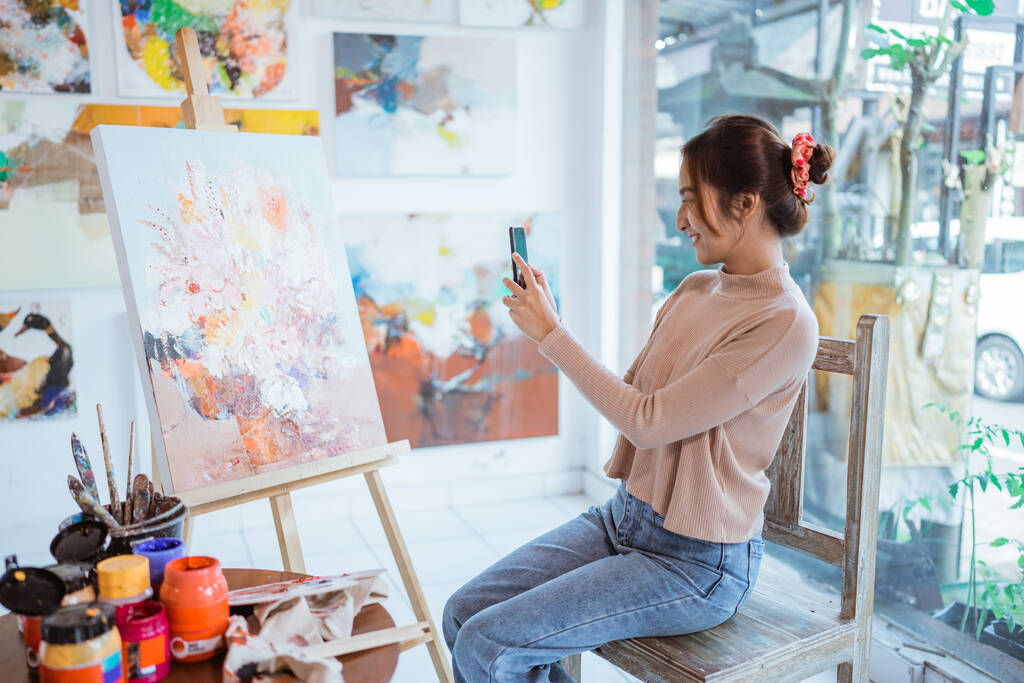 アジアの女性アーティストがスマートフォンで自分の絵を撮影し - 写真・画像