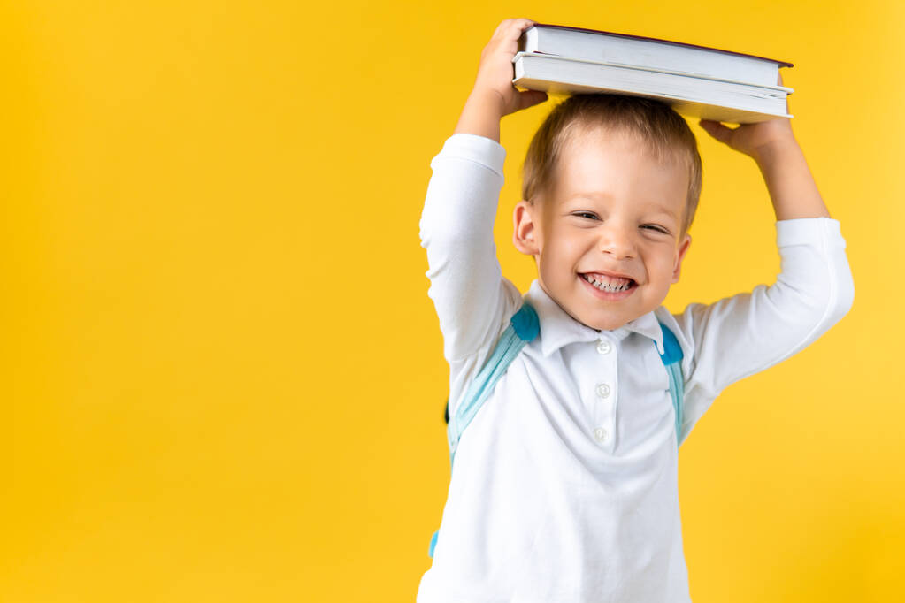 Banner Funny Prechool Child Boy 3-4 years with Book on Head and Bag on Yellow Background Copy Space. Счастливого Улыбающегося Малыша, возвращайся в школу, детский сад. Сукчес, Мбаппе, Гений, Супергерой - Фото, изображение