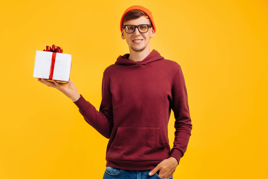 feliz joven en sombrero naranja con gafas y suéter rojo demuestra su regalo, humor festivo, descuentos de otoño, venta en línea - Foto, Imagen