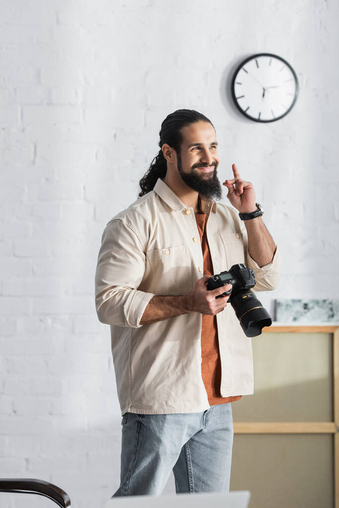 joyful hispanic man with digital camera showing idea sign while standing at home - Photo, Image