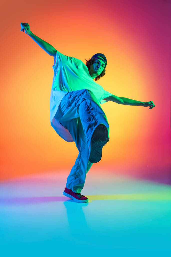 Retrato conceptual de joven, bailarín de hip-hop en ropa elegante en acción aislado sobre fondo colorido en salón de baile en luz de neón. - Foto, Imagen