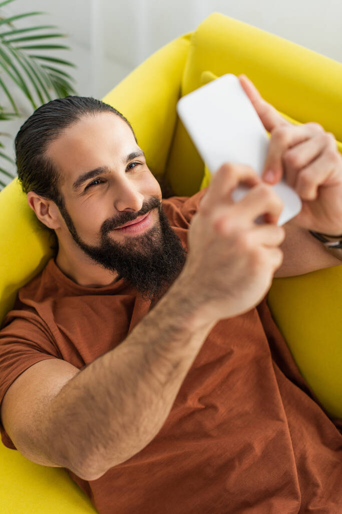 alto ángulo vista barbudo hispano hombre tomando selfie en borrosa teléfono móvil - Foto, imagen