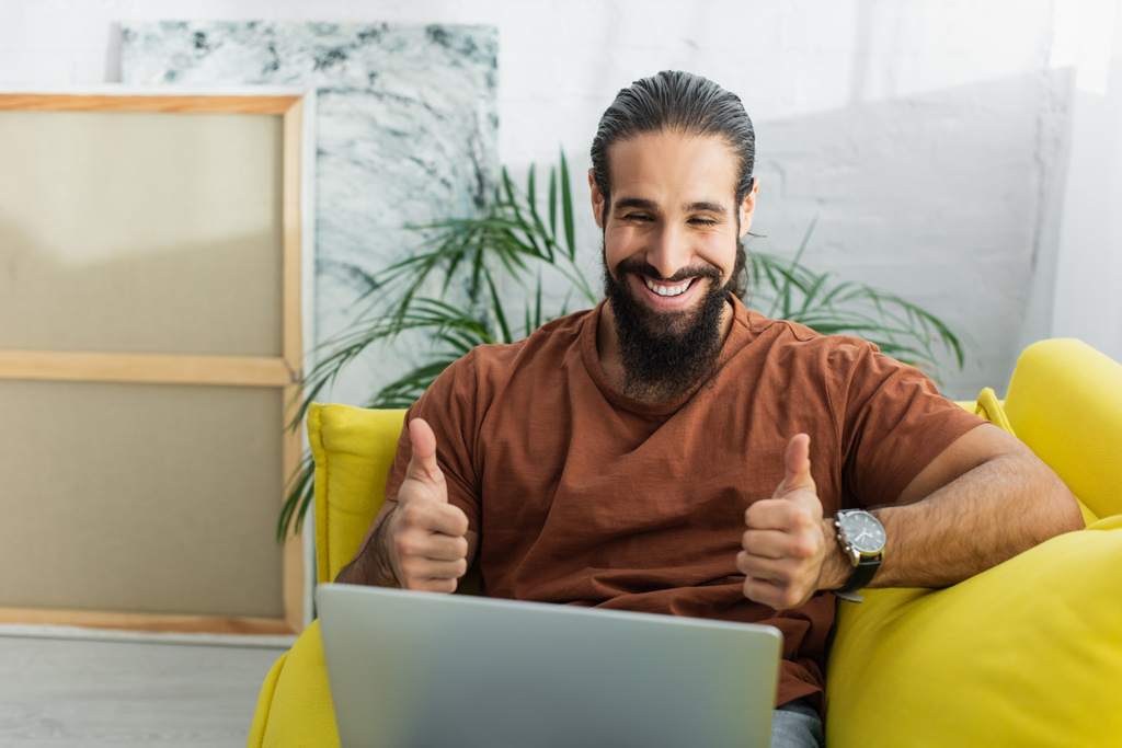 hombre hispano feliz mostrando los pulgares hacia arriba durante el chat de vídeo en el ordenador portátil en casa - Foto, Imagen