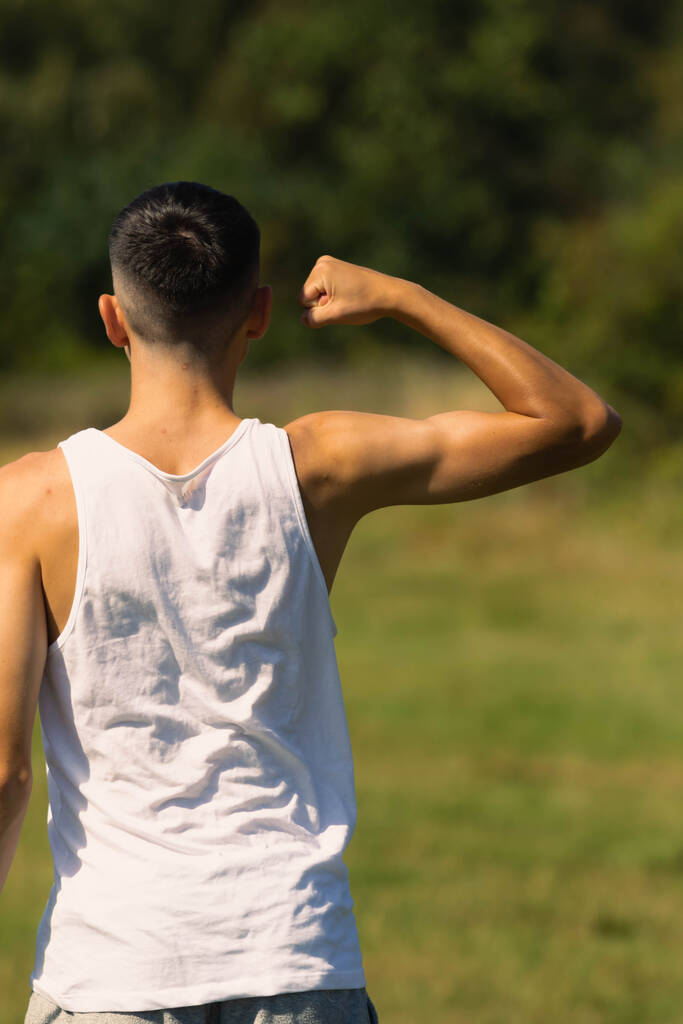 18 yaşında kolsuz tişörtlü bir genç yaz günü kol kaslarını esnetiyor. - Fotoğraf, Görsel