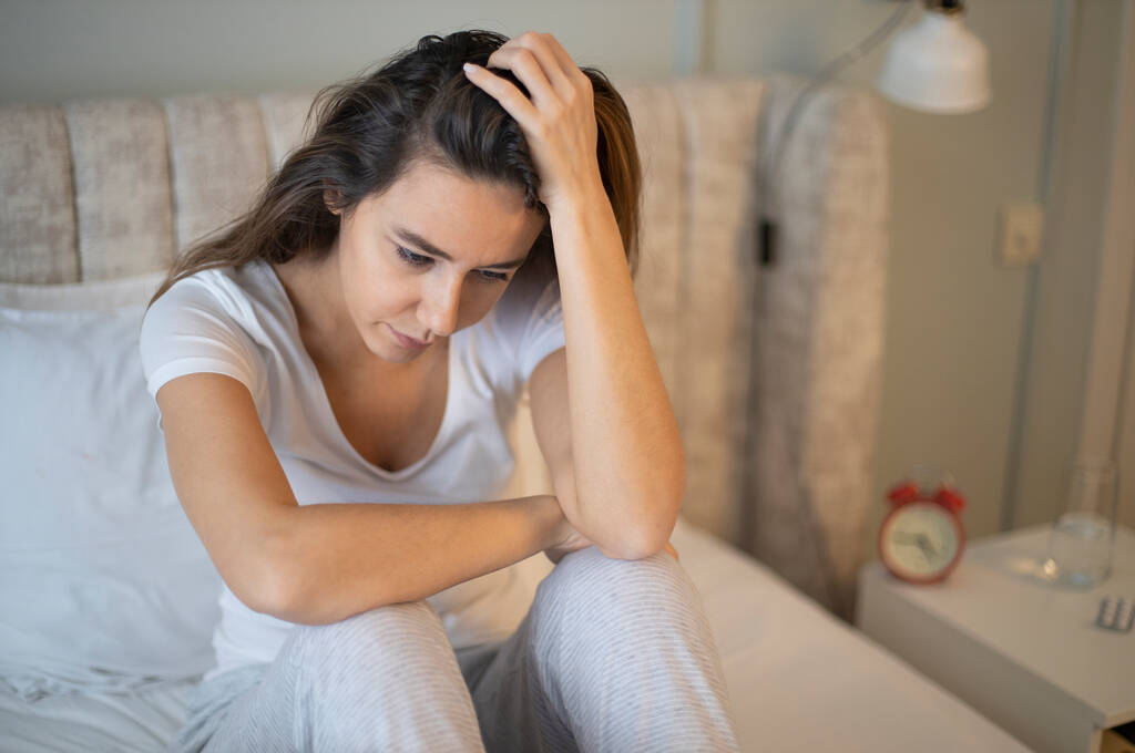 Surullinen masentunut nainen kärsii unettomuus, hän istuu sängyssä ja koskettaa päätään, unihäiriö tai stressi käsite - Valokuva, kuva