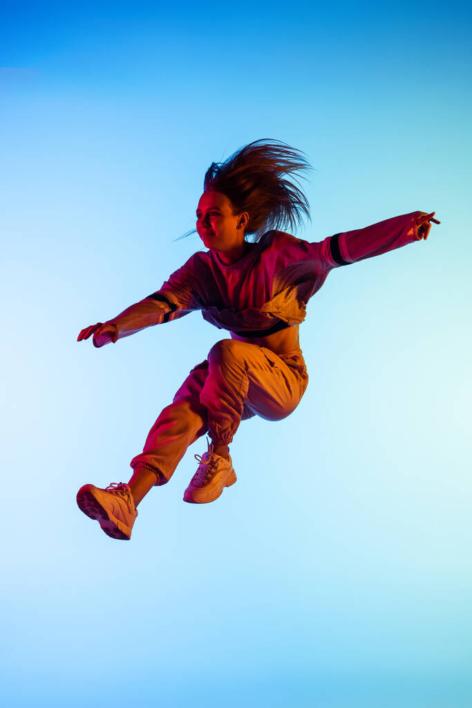 Una giovane ragazza sportiva danza hip-hop in abiti eleganti su sfondo colorato alla sala da ballo in luce al neon. Cultura giovanile, movimento, stile e moda, azione. - Foto, immagini