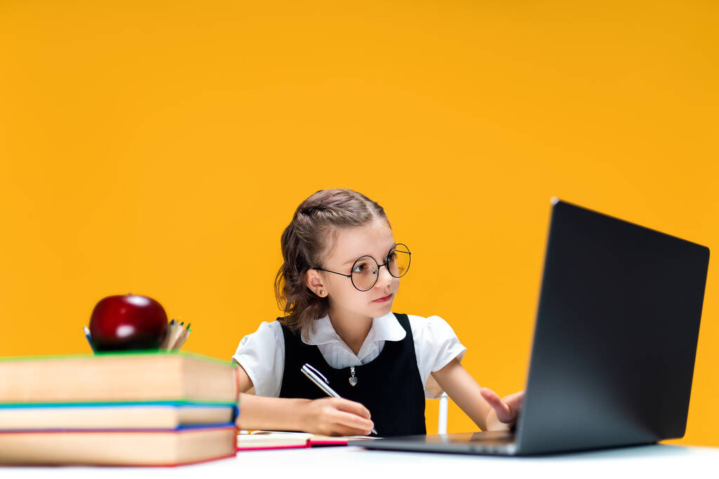 眼鏡を書き、オンラインレッスン中にノートパソコンに座っている女子高生。遠隔学習. - 写真・画像