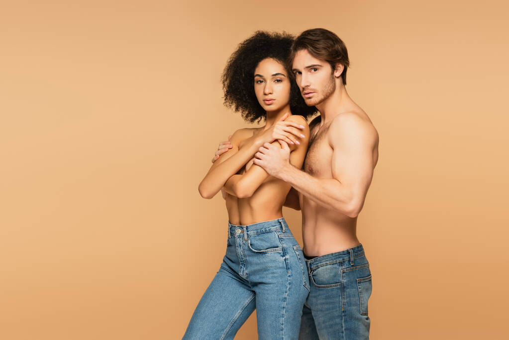 sensueel interraciaal paar in jeans alleen op zoek naar camera geïsoleerd op beige - Foto, afbeelding