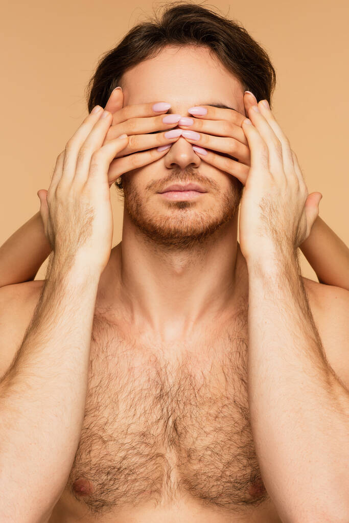 uomo senza maglietta toccando le mani di giovane donna oscurando i suoi occhi isolati sul beige - Foto, immagini