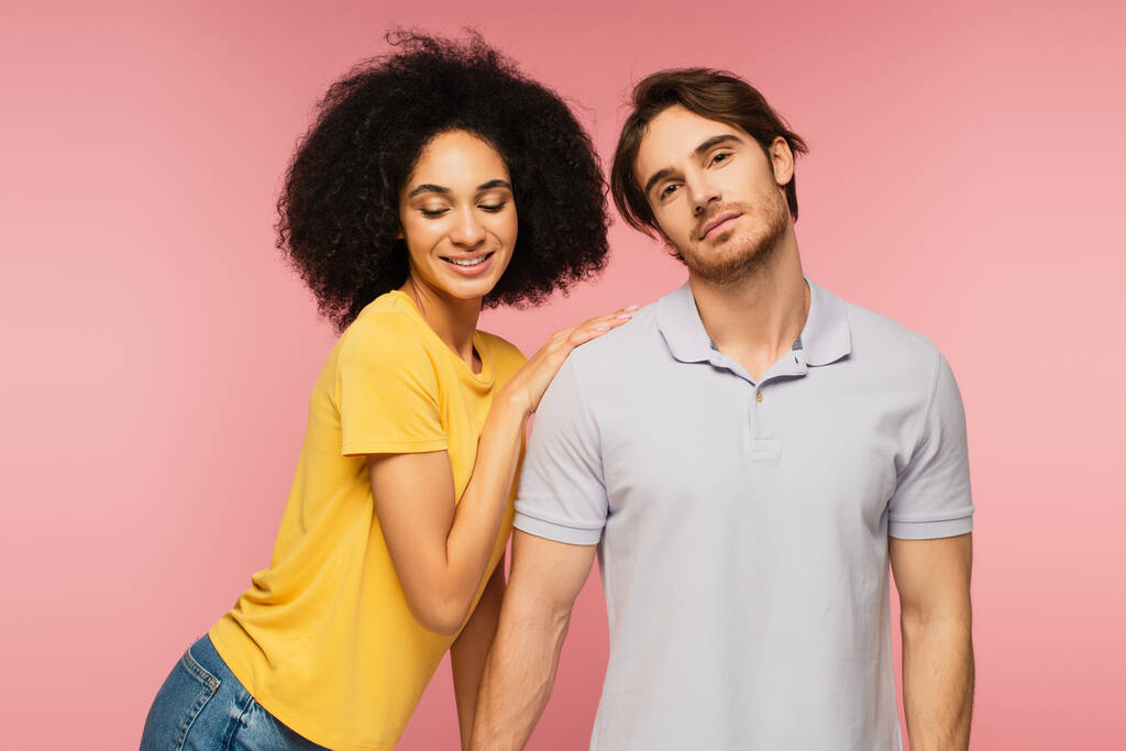 curly hispanic woman leaning on shoulder of young man looking at camera isolated on pink - Photo, Image