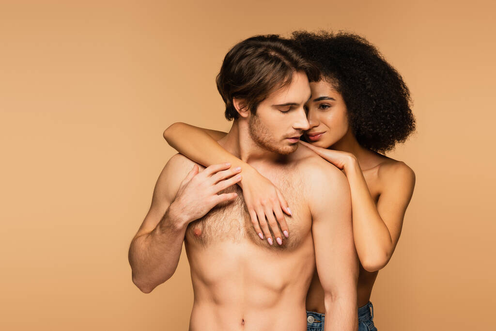 jovem hispânico mulher abraçando shirtless homem com muscular torso isolado no bege - Foto, Imagem