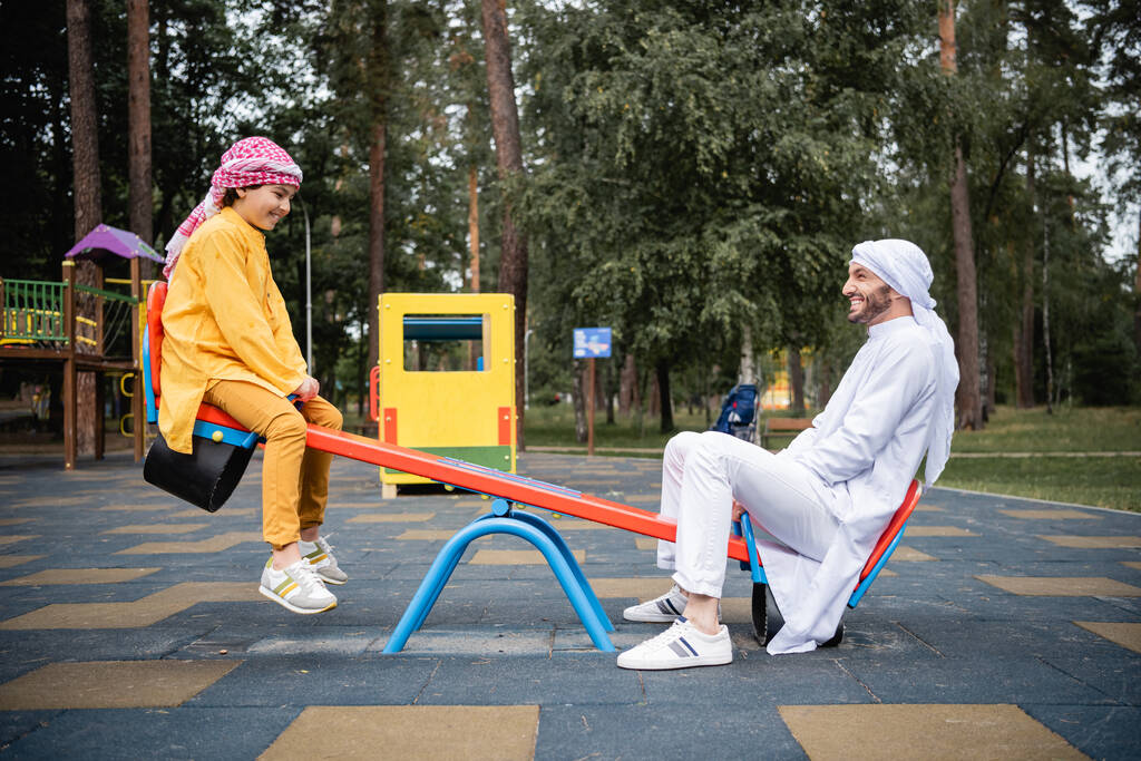 公園で遊び場で遊ぶアラビア人の息子と父親の側面図 - 写真・画像