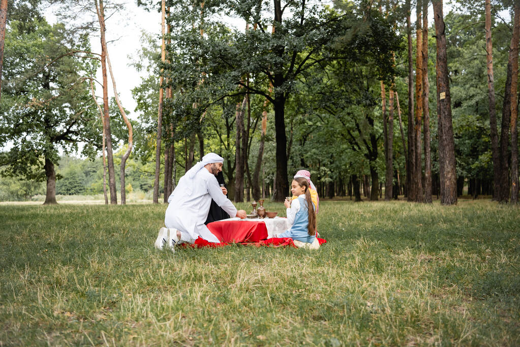 Pozitív arab apa ül közel a család piknik alatt a parkban  - Fotó, kép