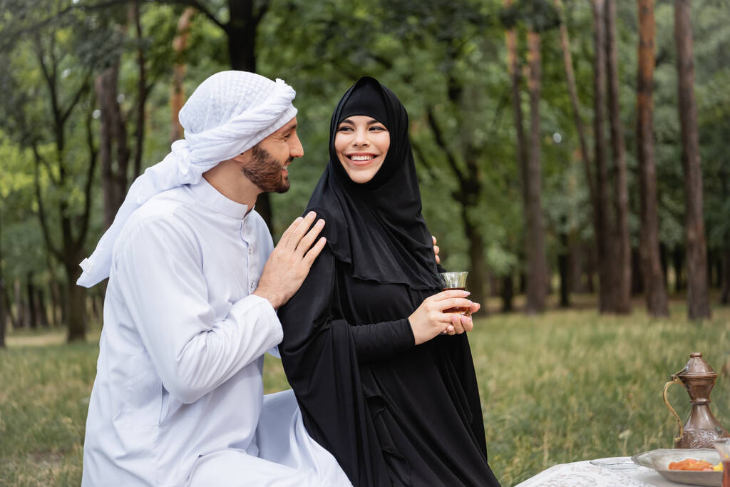 Árabe homem abraçando esposa no hijab segurando chá no parque  - Foto, Imagem