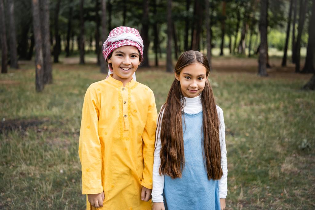 Muslimischer Junge in Kufiya lächelt in Kamera neben Schwester im Park  - Foto, Bild