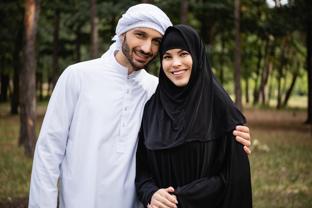 Pareja musulmana en ropa tradicional sonriendo a la cámara al aire libre - Foto, Imagen