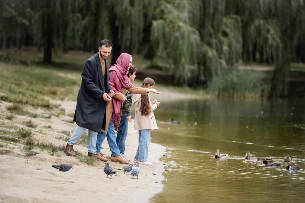 Happy muslim family looking at birds on lake  - Photo, Image
