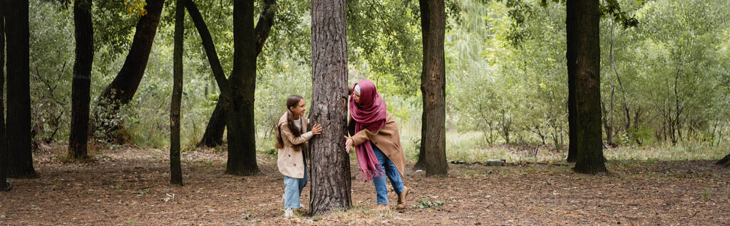 Улыбающаяся арабская девушка, играющая с матерью возле дерева в парке, баннер  - Фото, изображение