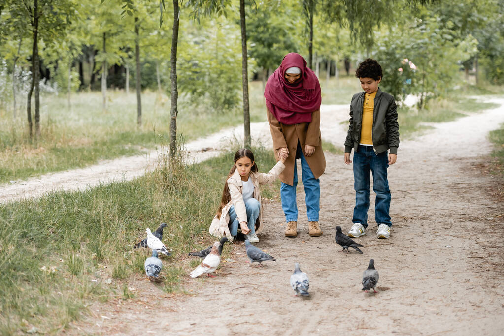 Parkta kuşların yanında duran Arap anne ve çocuk.  - Fotoğraf, Görsel