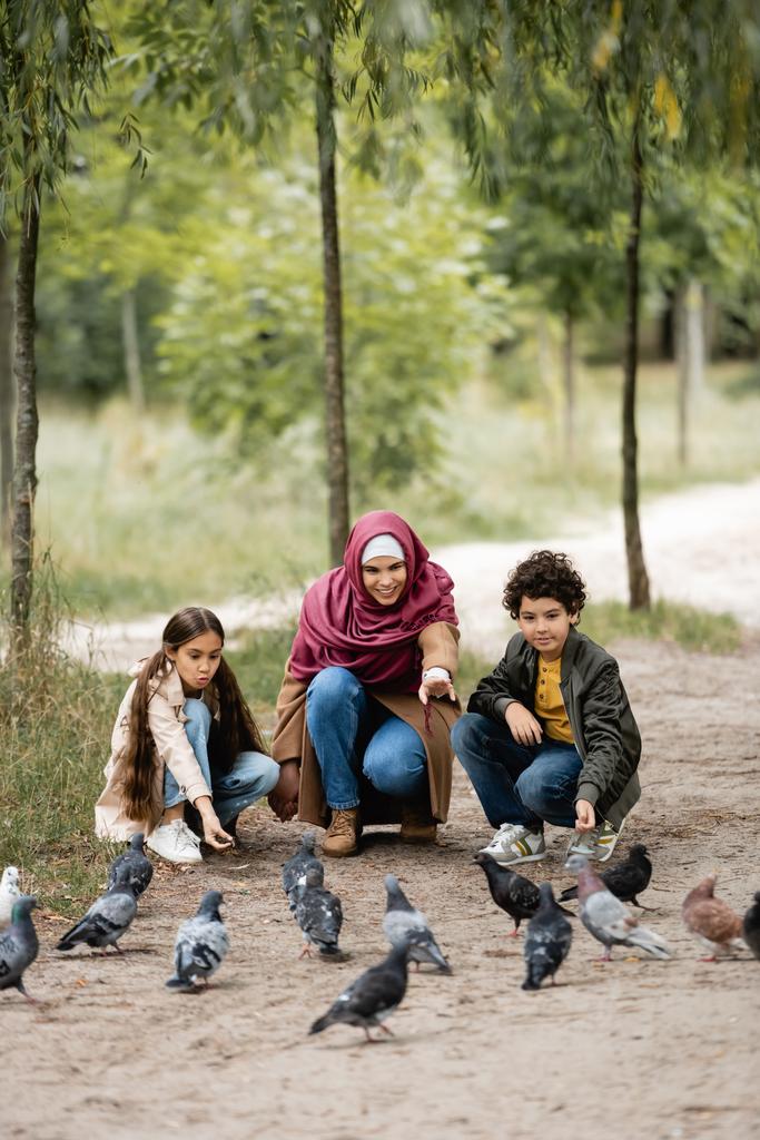 Muslimische Frau zeigt auf Vögel in Nähe von Kindern im Park  - Foto, Bild