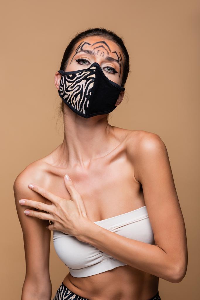 женщина с макияжем тигра и защитной маской для печати животных позирует изолированно на бежевом - Фото, изображение