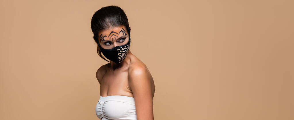 Kaplan makyajlı ve hayvan desenli koruyucu maskeli bir kadın bej pankartta tek başına bakıyor. - Fotoğraf, Görsel