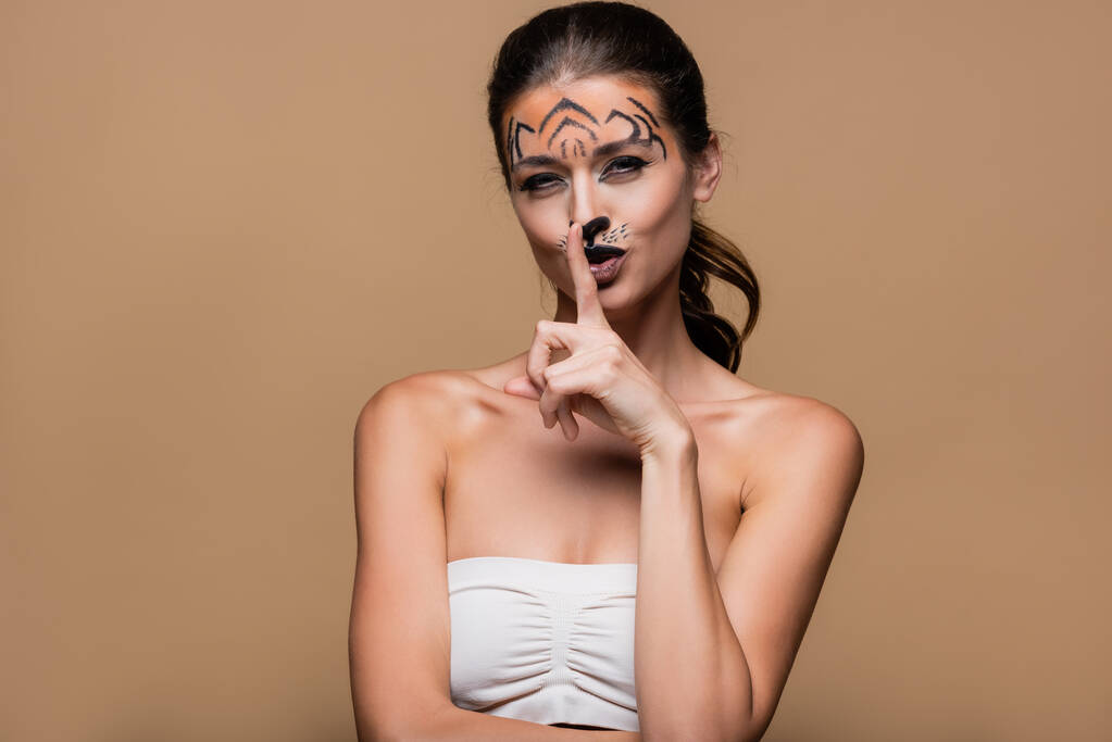 junge Frau mit nackten Schultern und Tiger-Make-up zeigt Schweigezeichen isoliert auf beige - Foto, Bild