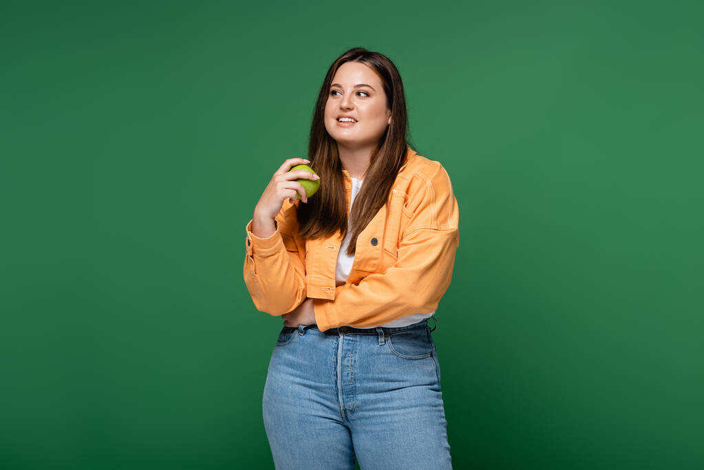 Улыбающаяся женщина с избыточным весом держит яблоко изолированы на зеленый  - Фото, изображение