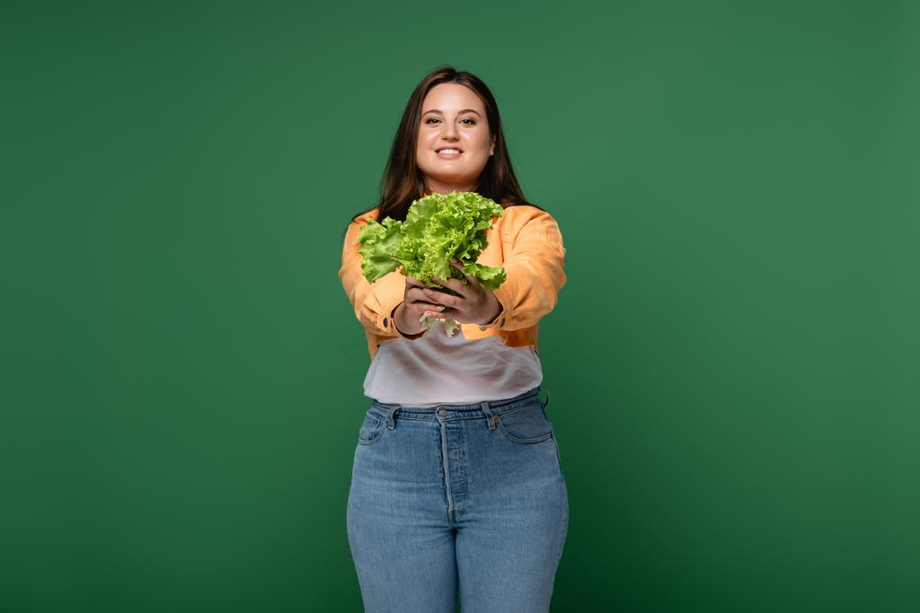Usmívající se žena s nadváhou drží salát izolovaný na zelené  - Fotografie, Obrázek