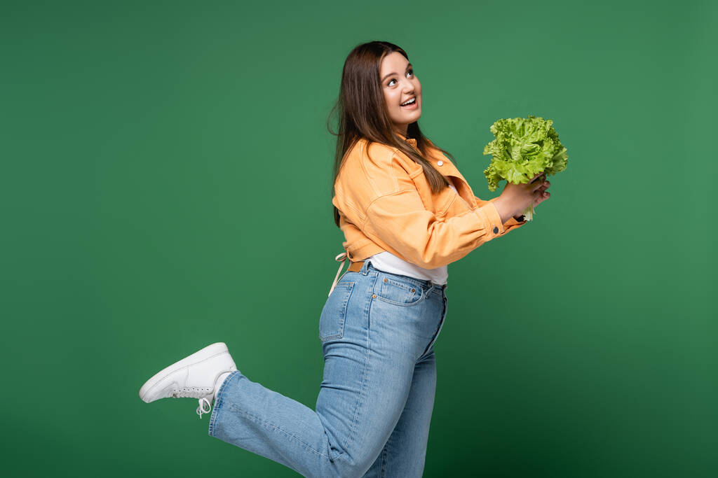 Happy woman with overweight holding lettuce isolated on green  - Photo, Image