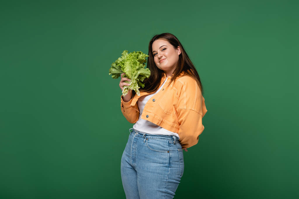 Jovem corpo positivo mulher segurando alface fresca isolada em verde  - Foto, Imagem
