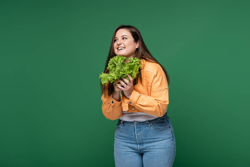 Ευτυχισμένη γυναίκα με υπέρβαρα κρατώντας φρέσκο μαρούλι απομονωμένο στο πράσινο  - Φωτογραφία, εικόνα