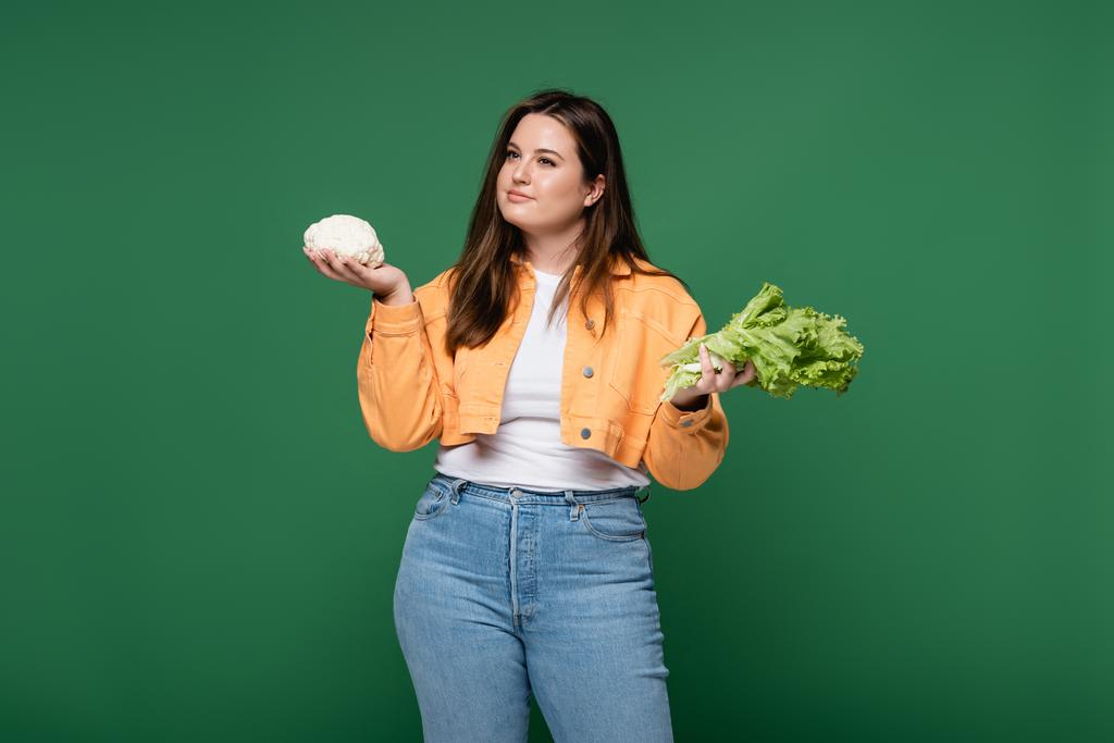 Όμορφη γυναίκα με υπέρβαρη εκμετάλλευση κουνουπίδι και μαρούλι απομονώνονται στο πράσινο  - Φωτογραφία, εικόνα