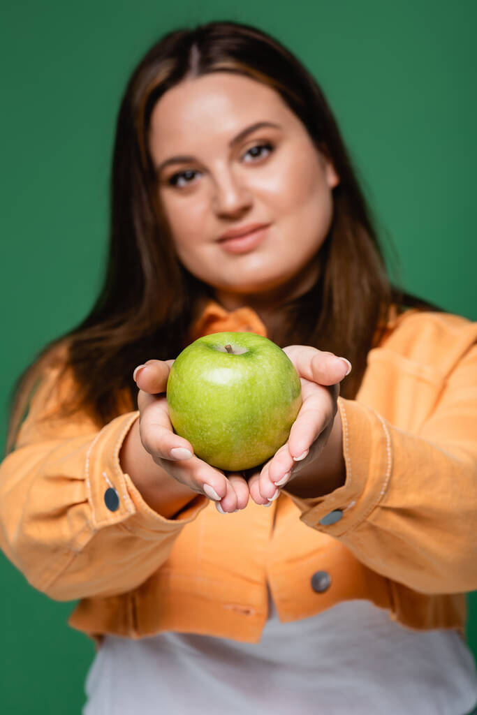 Manzana en manos de mujer con sobrepeso sobre fondo borroso aislado sobre verde  - Foto, Imagen