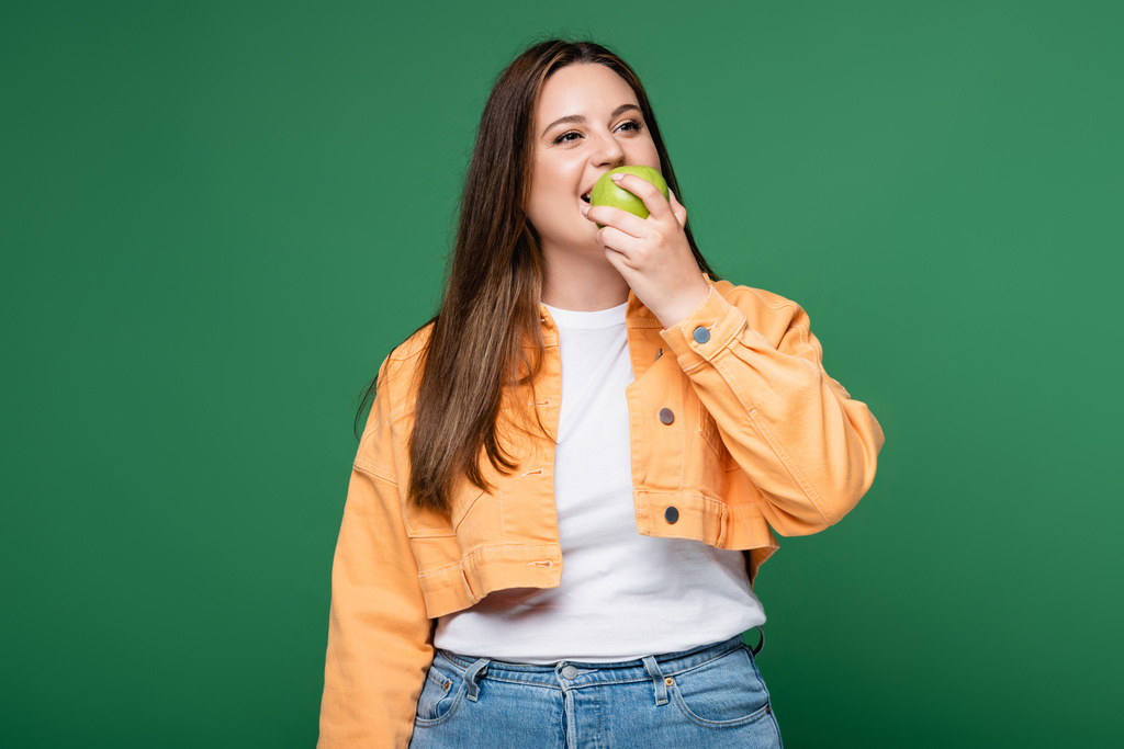 Jeune femme avec un excès de poids manger pomme isolé sur vert - Photo, image