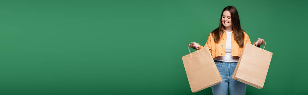 Щаслива жінка з надмірною вагою тримає сумки ізольовані на зеленому, банер
  - Фото, зображення