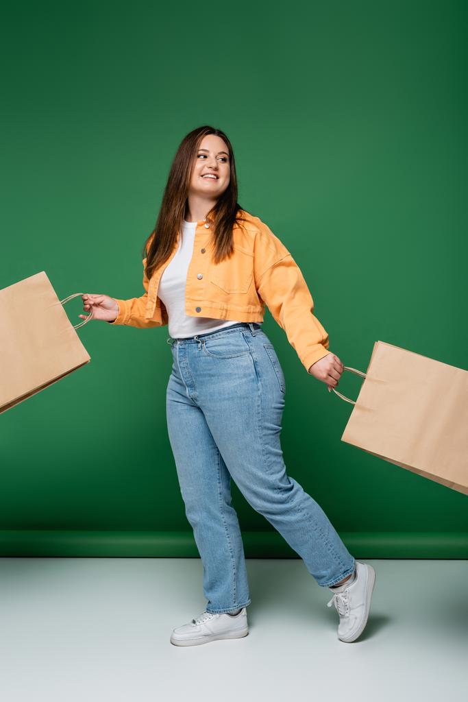 Веселое тело позитивная женщина с ремесленными сумки ходить на зеленом фоне - Фото, изображение