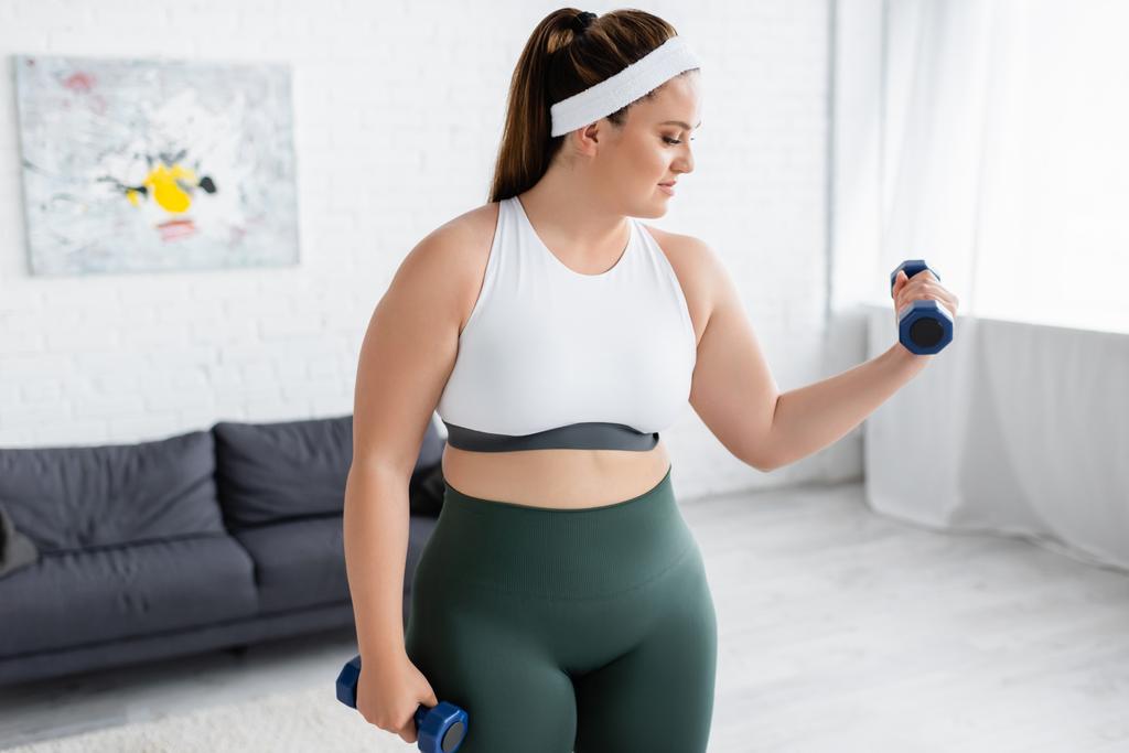 Side view of plus size woman training with dumbbells in living room  - Photo, Image