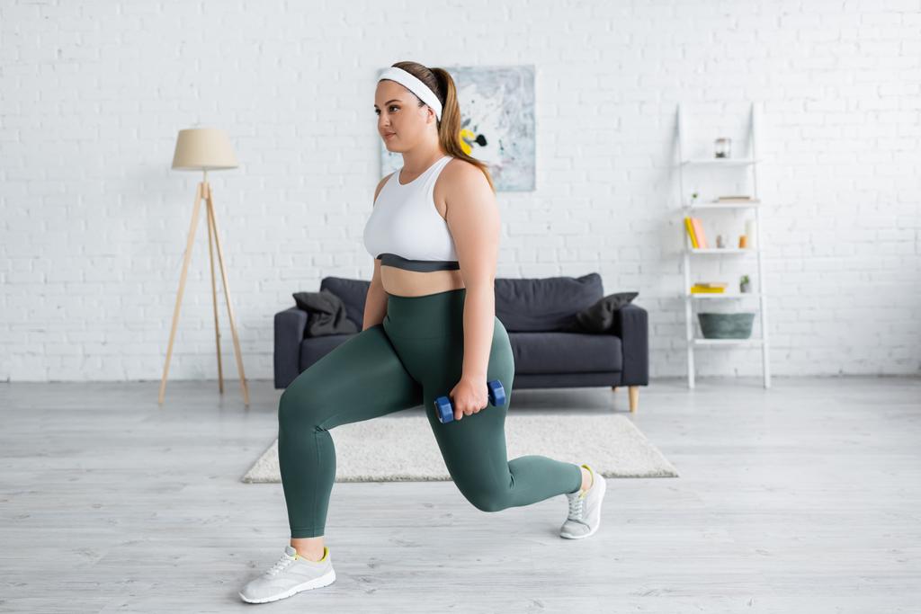 Brunette woman with overweight doing lunges with dumbbell at home  - Photo, Image
