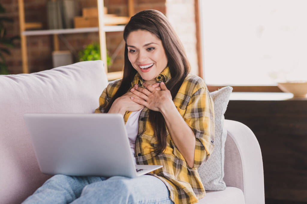 興奮した女性の写真快適なソファを保持するノートパソコンの手胸を着用再生シャツホーム屋内に座る - 写真・画像