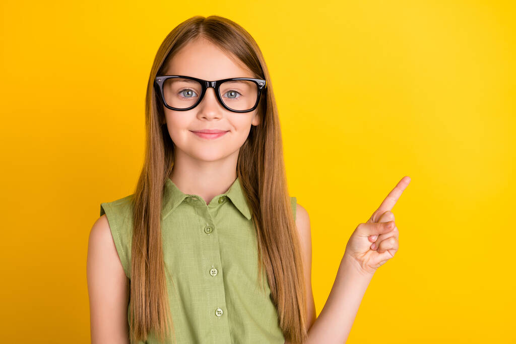 Fénykép okos szőke kislány pont üres tér viselet szemüveg khaki blúz elszigetelt sárga színű háttér - Fotó, kép