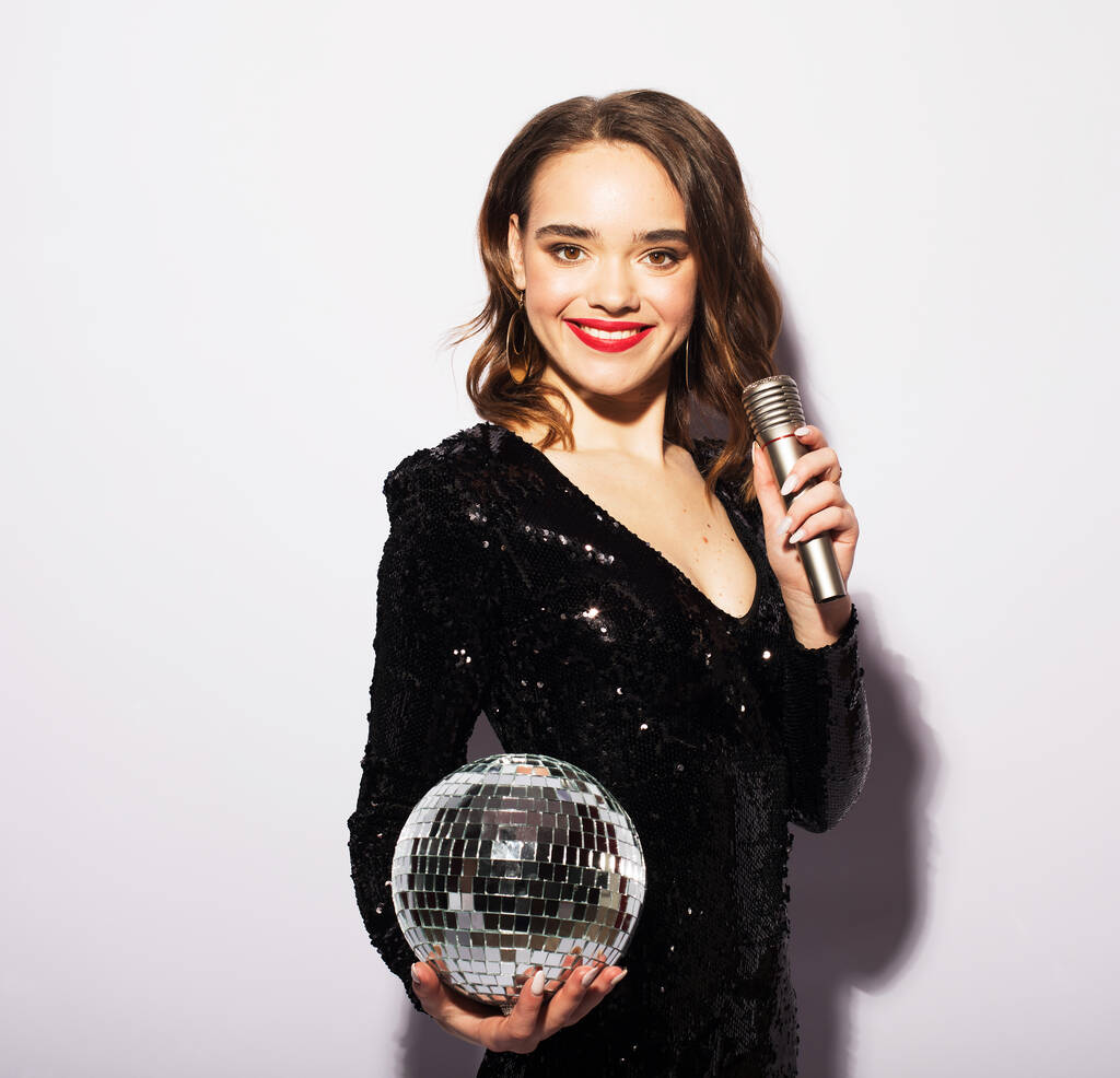 Beautiful woman holding a microphone and disco balls over white background. - Photo, Image