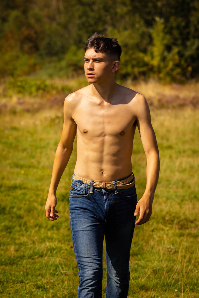Een 18-jarige tienerjongen die op een warme zomerdag in een park loopt terwijl hij zonder shirt - Foto, afbeelding
