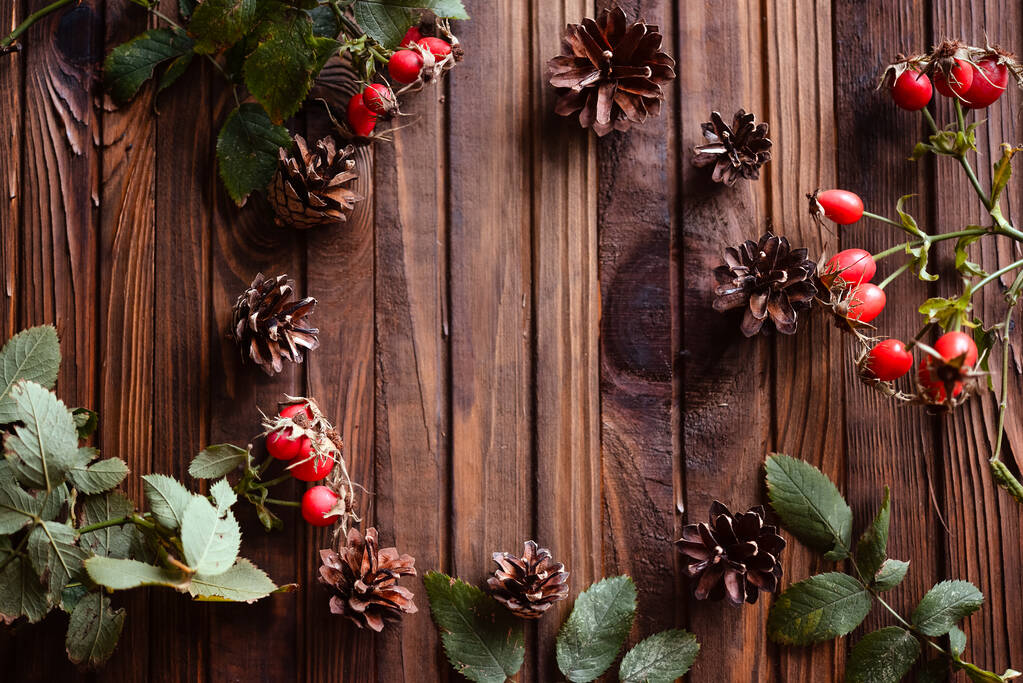 Vánoční dekorace na dřevěném pozadí. Šišky, jehly, růžové boky. Teplá a útulná pohlednice. - Fotografie, Obrázek