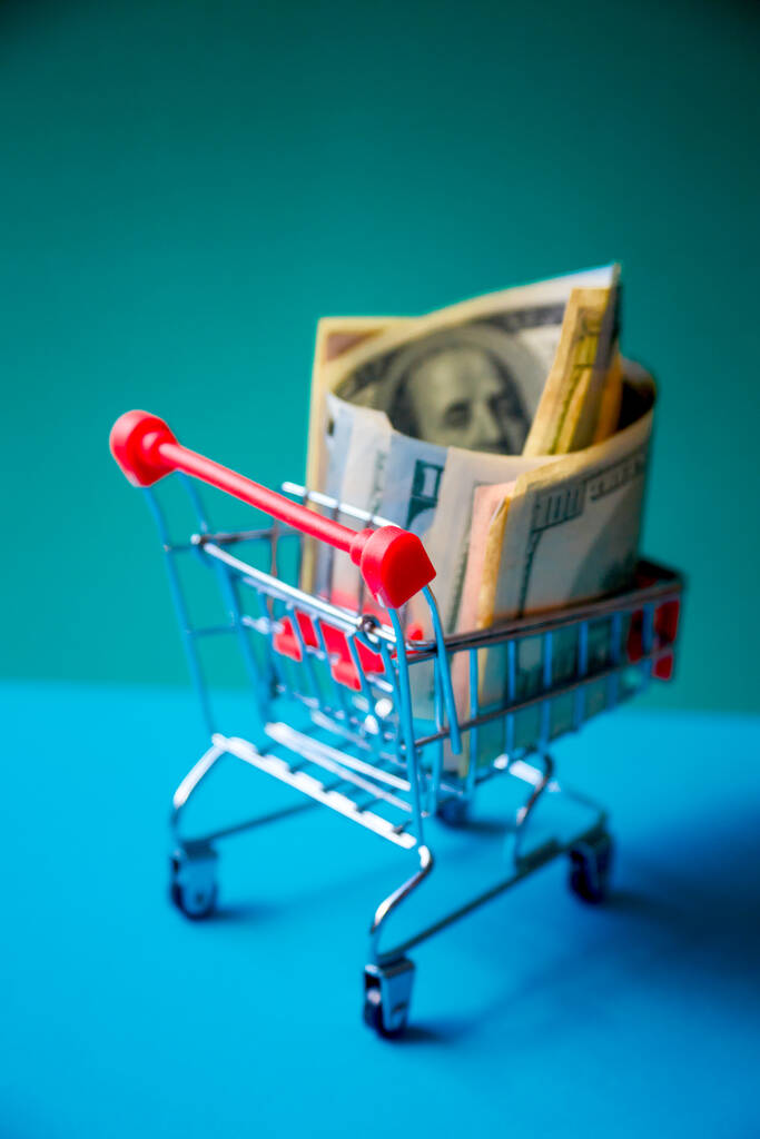 concept - curled dollar banknotes lie in Shopping Cart Trolley against the green background - Photo, Image