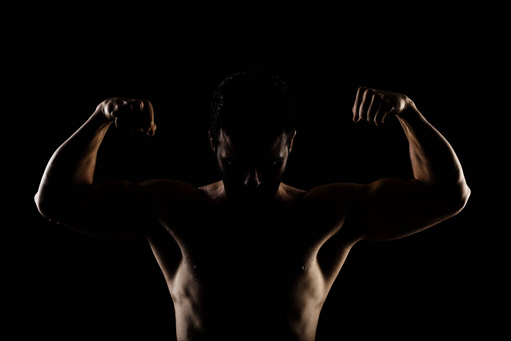 Sílhueta de homem caucasiano musculoso com iluminação lateral. Atleta posando contra fundo preto.  - Foto, Imagem