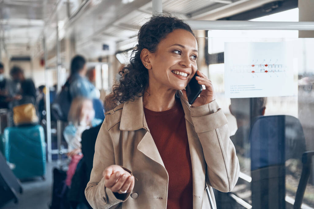 Красивая зрелая женщина с помощью смартфона и улыбаясь во время путешествия на поезде - Фото, изображение