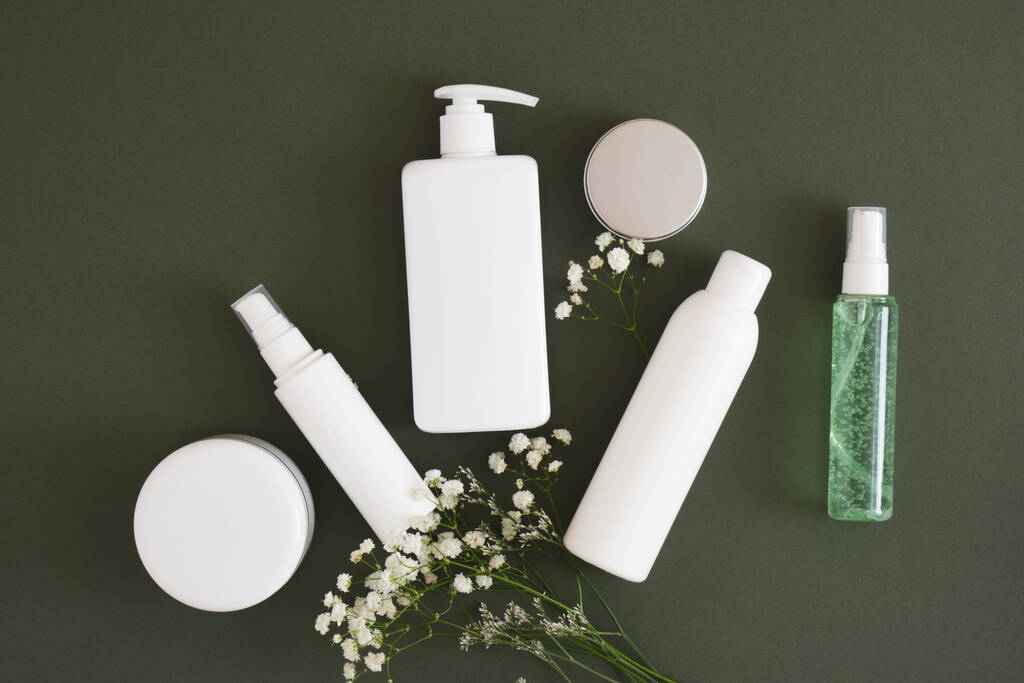 flowers, different cosmetic jars and three different blank white bottles on a dark green background backdrop Natural cosmetic packaging. mock up beauty product concept. - Photo, Image