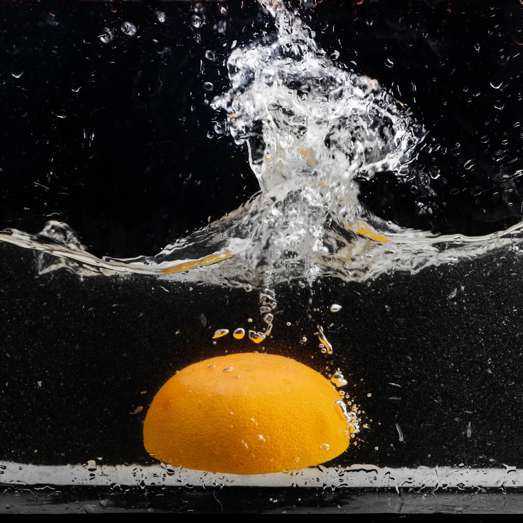 Tuore puoli appelsiini, viipaleita putoaa veteen tilkka vettä ja ilmakuplia, eristetty mustalla pohjalla. - Valokuva, kuva